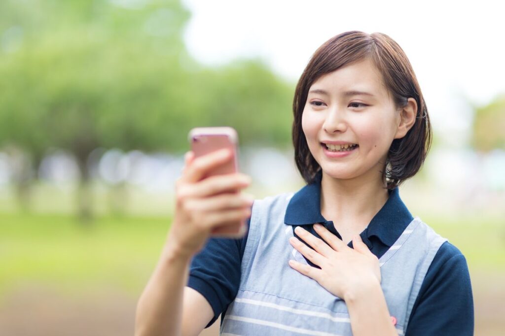 公園でスマホを見ながら子どもの位置を確認する母親。子ども用GPSを使うシーンのイメージ。