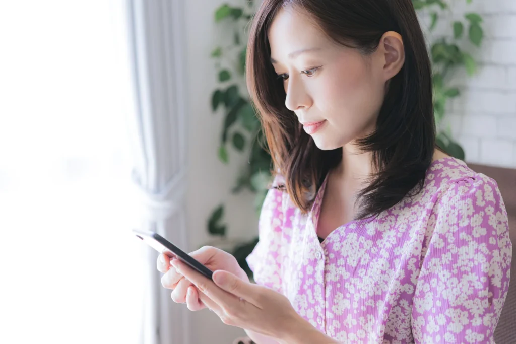 室内でスマホを見ながら子どもの位置を確認する母親。子ども用GPSを使うシーンのイメージ。