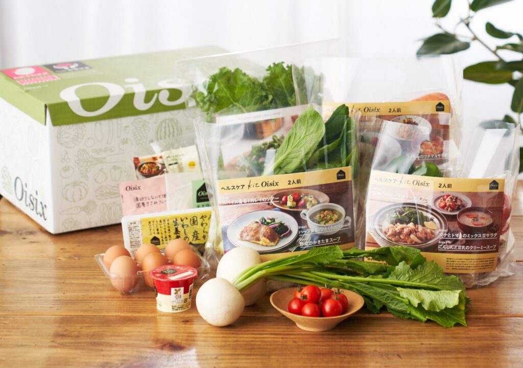 Oisixお試しセットの箱と新鮮な野菜やミールキットがテーブルに並んでいる写真
